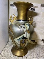 Full view of the vintage ceramic vase showing Picasso style abstract face designs with gold handles and accents, set on a countertop against a tile backsplash.