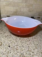 Large red Pyrex mixing bowl with white interior, shown front angle on kitchen counter.