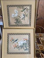 Two framed vintage Asian watercolor paintings on silk, stacked vertically showing delicate floral and bird scenes within patterned borders.