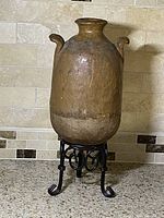 Front angled view of the vintage pottery jug/vase showing its shape, textured brown glaze, and metal stand.