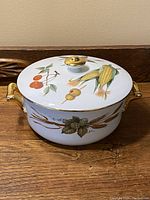 Front view of vintage Royal Worcester porcelain bowl with lid showing painted fruit and corn design, and gold-tone handles and lid knob.
