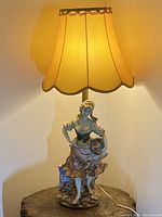 Full view of the vintage table lamp lit showing the yellow fabric shade and hand-painted figurine base depicting a girl.