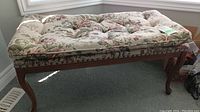 Full side view of tufted floral upholstered bench showing wooden legs and frame with brass tacks and gimp trim.