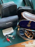 Image showing multiple binocular cases including Bushnell and a brown leather case with Tasco opera glasses inside lined with purple velvet.