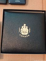 Closed presentation case, black textured exterior with gold Canadian crest