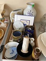Overview of assorted porcelain and ceramic vases, plates, and decorative china pieces packed in a box.