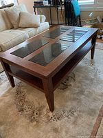 Angled front side view of rectangular coffee table showing four black stone inlays embedded in wood veneer top and lower storage shelf.