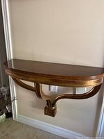 Front view of the half-circle wooden wall shelf with gold-accented curved support bracket mounted on beige wall.