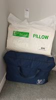 White Nikken Kenko Dream pillow sealed in original plastic packaging and navy blue Nikken storage bag with handles, presumably containing the duvet.