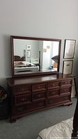 Full view of the solid mahogany dresser with matching mirror mounted on top, showing the front profile, brass drawer pulls, and the mirror reflecting the room's interior.