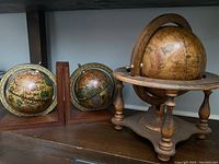 Wide shot showing the large wooden stand globe and two smaller bookend globes with antique map style.