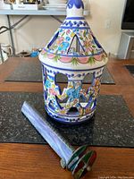 Glazed ceramic light cover with colorful painted floral and abstract patterns, and the handmade kaleidoscope laying beside it on the table.