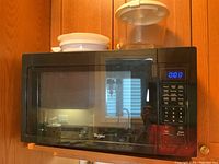 Black Whirlpool countertop microwave with turntable visible through door, placed against wood cabinetry.