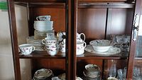 View of the mantelpiece cabinet shelf showing stacked plates of various sizes, teacups, and saucers with a floral bone china pattern and gold trim.
