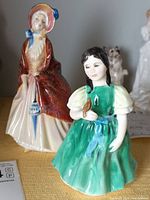 Side and front views of Francine HN 2422 figurine in green dress holding a bird, with Paisley Shawl figurine visible behind it