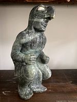 Front side view of the soapstone carving showing crouching figure with eagle head mask, details of face, arms, and feathers visible.