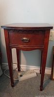 Front view of wooden side table showing scalloped detail and brass drawer pull.