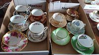 Full set of ten assorted vintage teacups with matching saucers displayed in two cardboard trays showing floral and gold-trimmed designs.