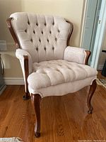 Front view of upholstered chair showing button tufted microsuede back and seat, wood trim and curved legs.