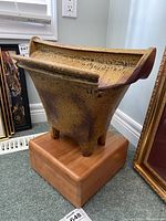 Front and side view of a glazed pottery urn on a wooden base, showing its shape, glaze, and feet