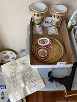Photo of both antique urns, decorative plates, vintage letter and partially visible tray inside cardboard box