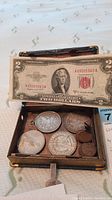 Two-dollar note displayed over box interior showing silver dollars and pennies