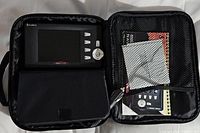 Portable DVD player inside a soft carrying case along with accessory cables and manuals in mesh pocket.