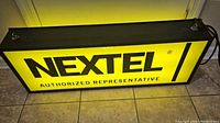 Nextel side of the illuminated advertising light box showing the brand text on a yellow background in black lettering.