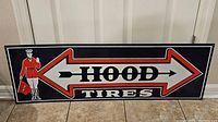 Full front view of the rectangular Hood Tires metal sign showing the man in red uniform and double arrow with brand text.