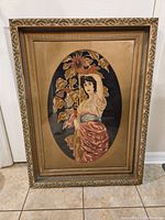 Full view of the framed large needlepoint tapestry showing the gold ornate frame and the woman with sunflowers design