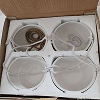 Top-down view of four white ceramic hanging planters neatly packed in white foam within a cardboard box, cords arranged inside.