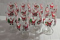 Eight clear glass stemmed glasses featuring a vintage Santa Claus holding a wreath design arranged in rows against a plain backdrop.