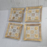 Four square Georges Briard glass dishes with mid-century gold and white decorative motifs photographed together.