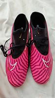 Top view of pair of Nike Phantom GX soccer cleats showing pink zebra striped pattern with white swoosh logos and black laces.