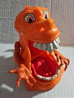 Close-up photo of the orange GooperGhost figure showing the front view with wide open mouth and large teeth, detailed hands, and expressive eyes.
