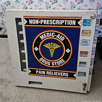 Front view of the Medic-Aid vintage medicine dispenser machine, showing logo, coin slots, key lock, and selection buttons.