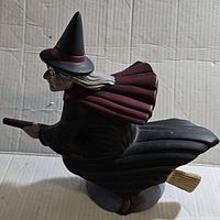 Side view of the witch flying on broom ceramic statue, showing the flowing cape and broom detail.