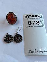 Photo showing large oval amber ring next to pair of silver earrings, display with auction lot card
