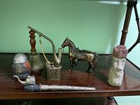 Full view of all items including bronze horse, brass bell with wooden handle, Asian brass pipe, Moai statue, Mate cup, and opium pipe.
