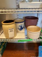 Four ceramic pots on a white wire shelf: two crocks (one blue and white, one beige with black interior) and two planters (brown and beige).