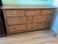 Full front view of wooden dresser showing seven drawers with mixed knobs including white patterned ceramic and dark round knobs.