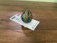 Emerald green decorative egg on a wood surface with a small tag beneath it.