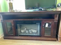 Front view of dark wood Napoleon electric fireplace TV stand with glass cupboard doors and upper shelf.