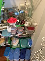 Overview of assorted kitchen storage items including plastic containers, glass jars, bottles, and lemon juicer on metal racks