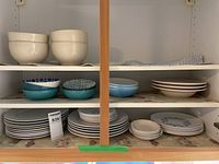 Shelves showing stacked cream-colored speckled bowls and serving bowls, patterned blue and white bowls, and assorted plates with blue floral and blue rim designs.