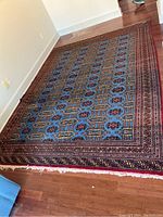 Full view of the large rectangular machine made area rug with blue central area and multi-colored borders on a wooden floor.