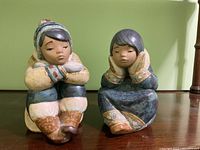 Front view of both Lladro Eskimo child figurines seated with hands on face