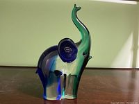 Front and side view of a colored Murano glass elephant figurine with translucent green and blue glass and rounded contours.