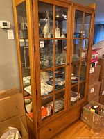 Full front view of oak display cabinet showing two glass front doors, interior shelving and lower drawer closed.