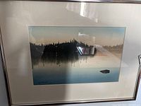Framed watercolour painting of a landscape with reflective water surface and distant tree line.